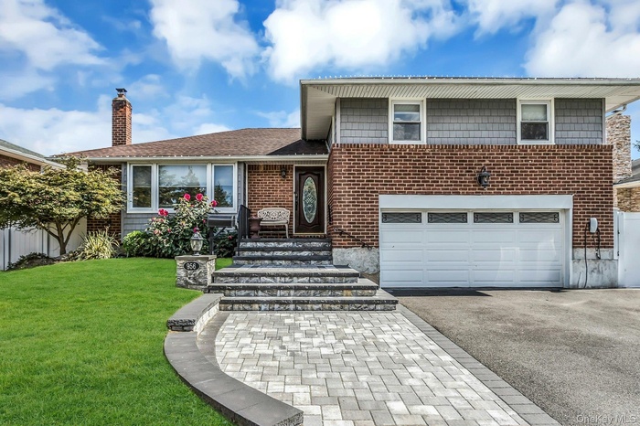 Split level home featuring asphalt driveway, a garage, a chimney, and brick siding