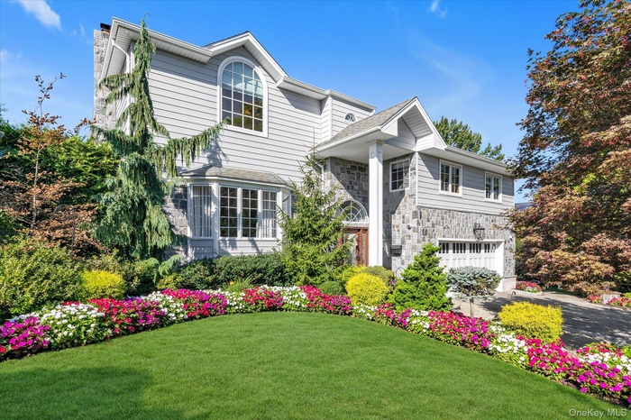 View of front of property featuring stone siding, a front yard, a chimney, a garage, and driveway