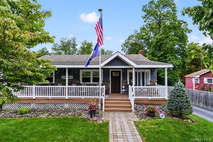 View of front of property featuring a chimney, a porch, a front yard, and stone siding