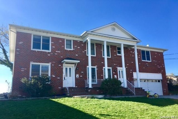 View of front facade with covered porch, a front yard, brick siding, and an attached garage