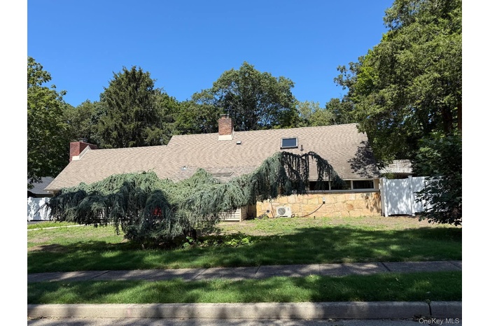 View of front facade with stone siding, a shingled roof, and a chimney