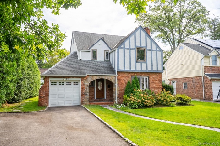 Tudor home with a front lawn, driveway, a shingled roof, and brick siding