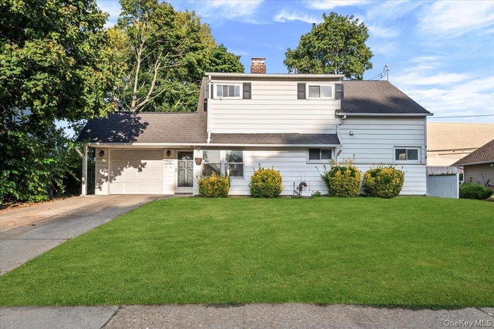 Traditional-style home with a front lawn, a chimney, an attached garage, concrete driveway, and roof with shingles