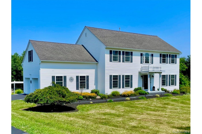 Colonial home featuring a front yard, roof with shingles, and an attached garage