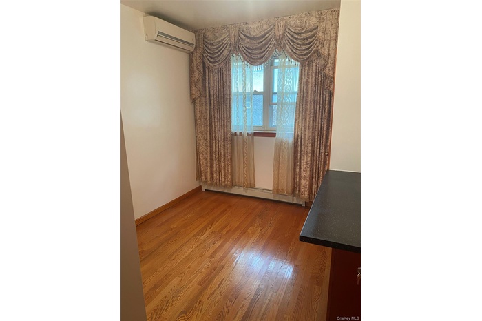 Empty room featuring light wood-type flooring, a wall unit AC, and a baseboard heating unit