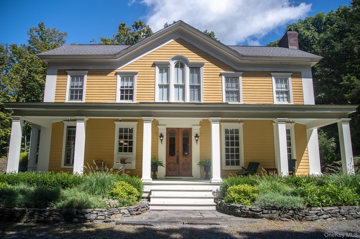 Greek revival inspired property featuring a chimney and covered porch