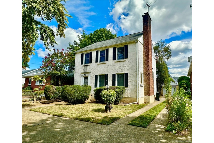 Colonial-style house featuring stucco siding, a chimney, and a front lawn