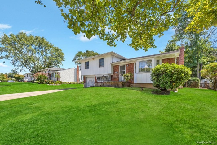 Split level home featuring a chimney, a front lawn, an attached garage, and brick siding