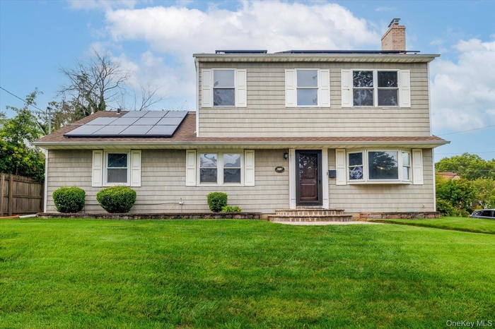 View of front of property with roof mounted solar panels, a chimney, and a shingled roof