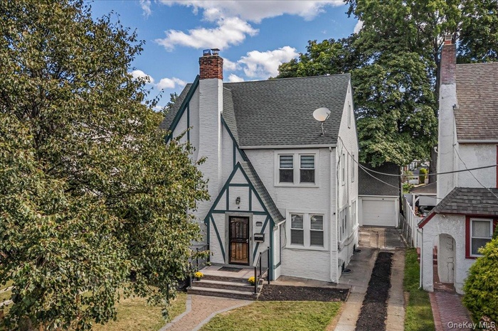 Tudor house with a shingled roof, a chimney, an outdoor structure, and driveway
