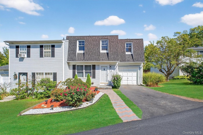 View of property featuring a front yard, roof with shingles, mansard roof, driveway, and a garage