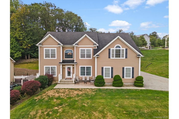 Traditional-style home featuring a front yard, roof with shingles, and a patio area