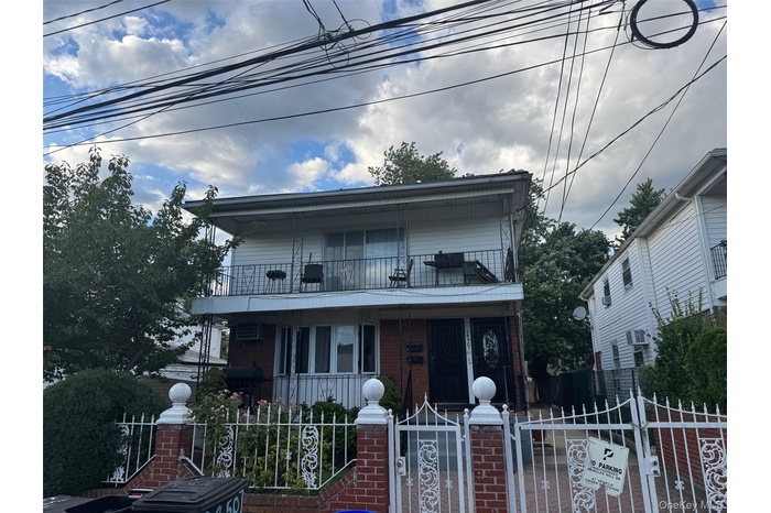 View of front facade with a gate, a fenced front yard, brick siding, covered porch, and a balcony