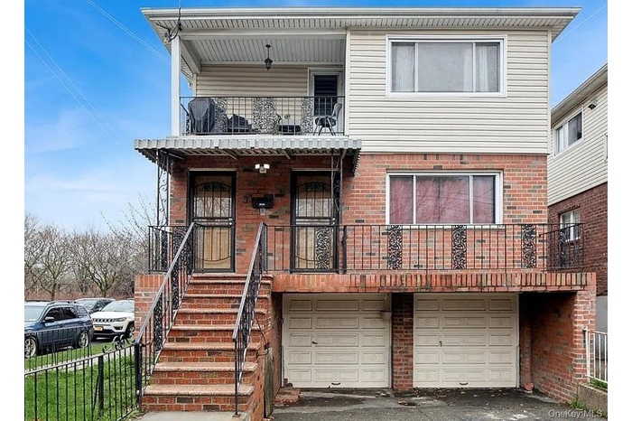 View of front of property featuring brick siding, a garage, a balcony, driveway, and a porch
