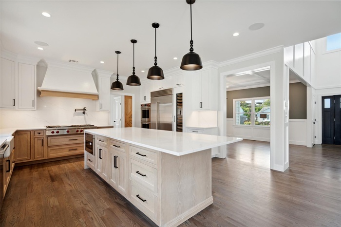 Kitchen with custom exhaust hood, built in appliances, light countertops, and dark wood-style floors
