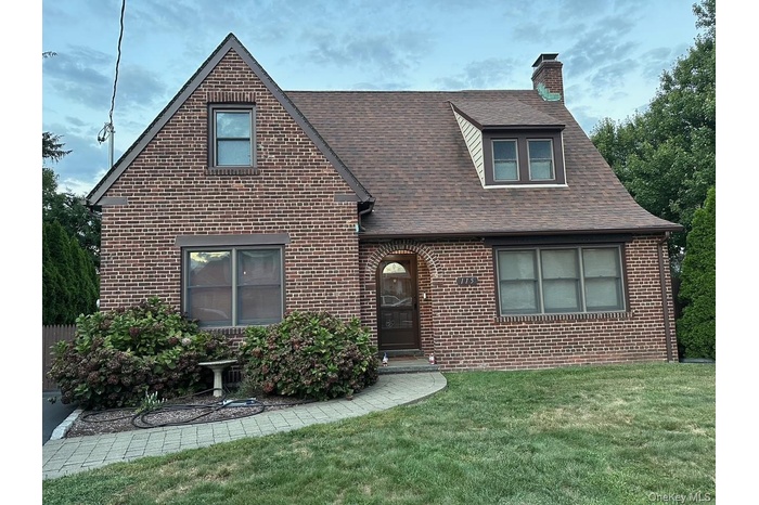 View of front of property with a front lawn, brick siding, a shingled roof, and a chimney