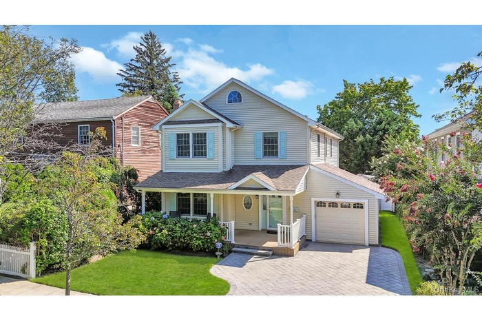 Traditional-style house featuring a porch, a shingled roof, a front yard, decorative driveway, and a garage