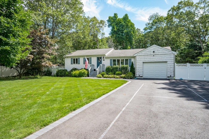 Ranch-style house with driveway, view of scattered trees, and an attached garage