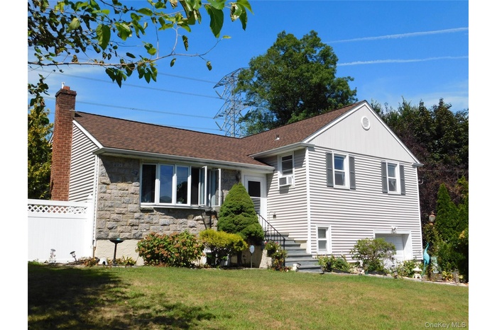 Split level home with stone siding, a shingled roof, a chimney, and an attached garage
