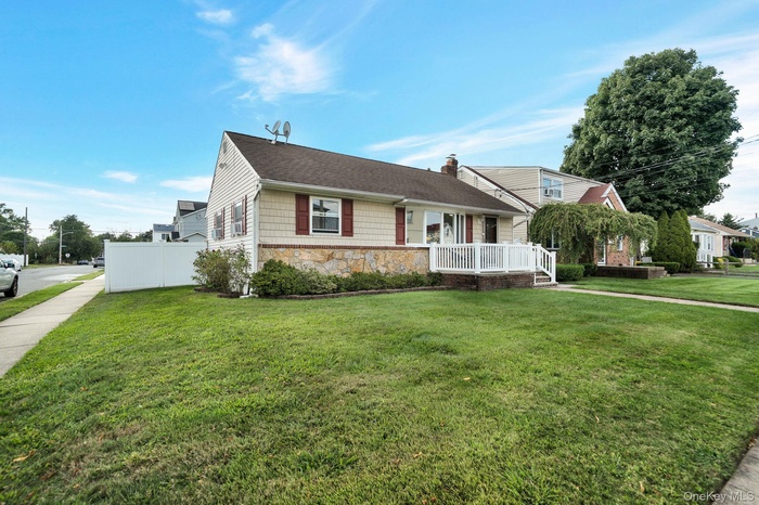 View of front of home featuring stone siding, a chimney, a shingled roof, and covered porch