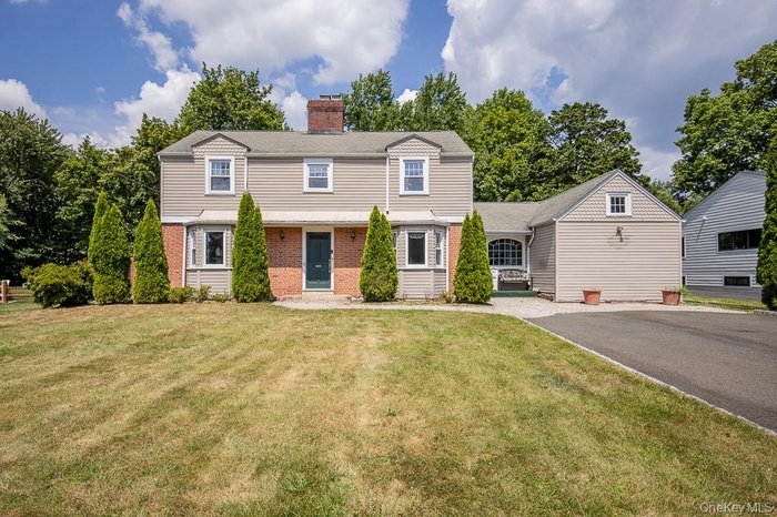 Colonial house with brick siding, a chimney, and a front yard