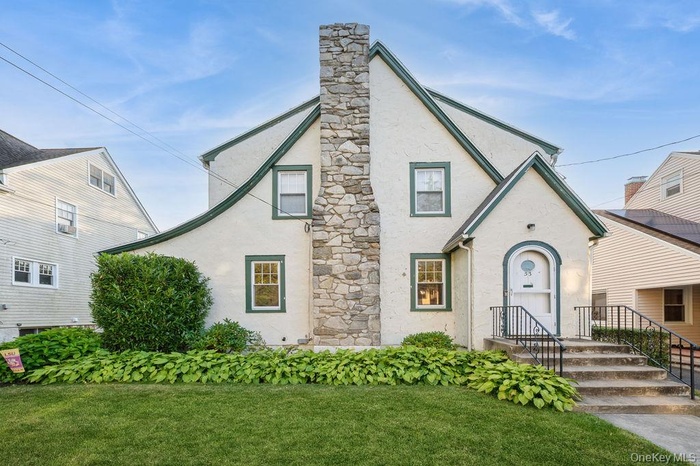 Tudor home featuring stucco siding, a front lawn, and a chimney