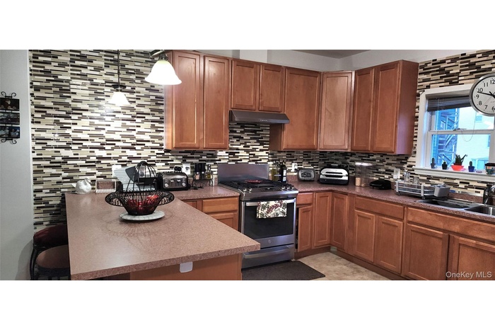 Kitchen with stainless steel gas stove, brown cabinets, tasteful backsplash, and under cabinet range hood