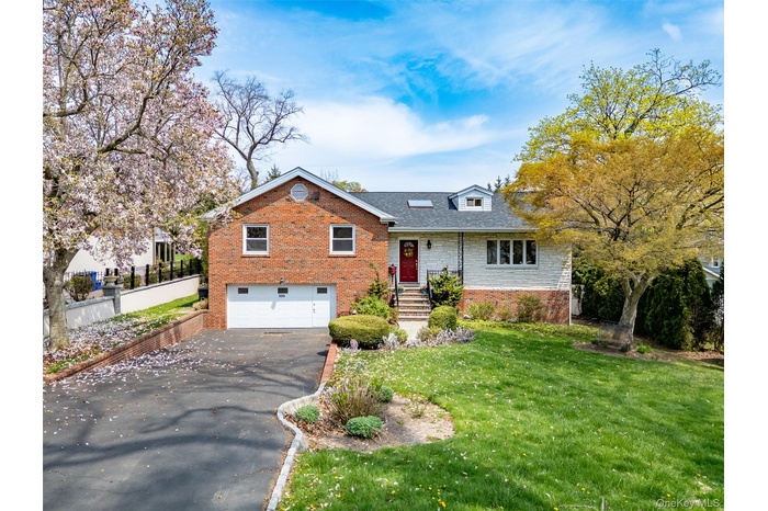 Split level home featuring brick siding, an attached garage, driveway, and a front yard
