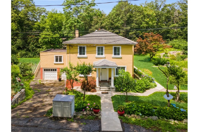 View of front of property featuring driveway, an attached garage, stucco siding, a chimney, and stairway