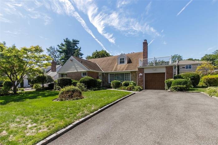 View of front facade with brick siding, a front lawn, driveway, a chimney, and an attached garage