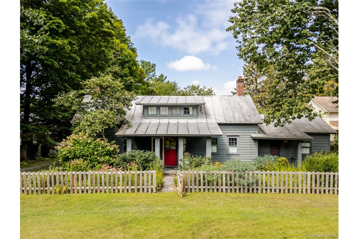 View of front facade with a fenced front yard, covered porch, a metal roof, and a chimney