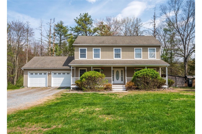 View of front of home with an attached garage, a front lawn, a porch, and gravel driveway
