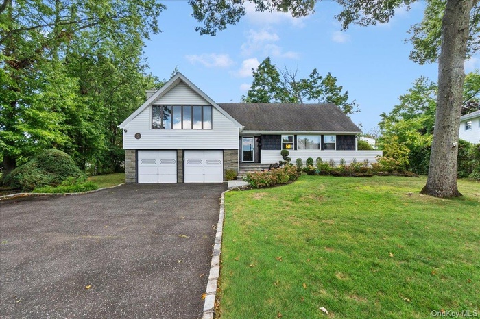 Tri-level home with asphalt driveway, stone siding, a front lawn, and an attached garage