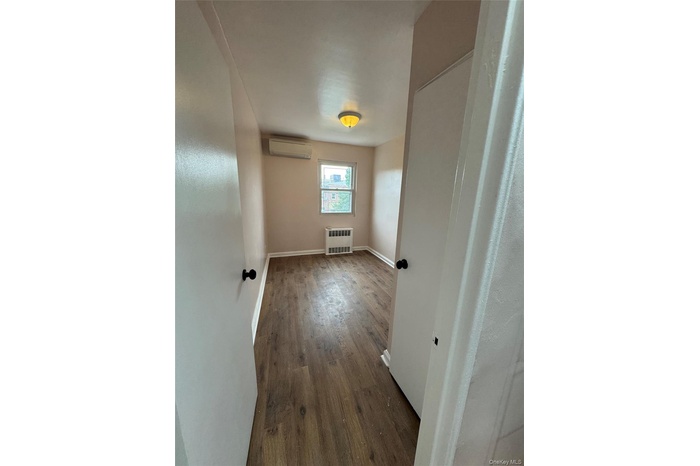Empty room with wood finished floors, radiator, and a wall mounted air conditioner