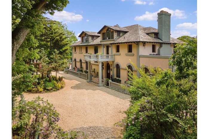 View of front facade with stucco siding, a balcony, a chimney, and curved driveway