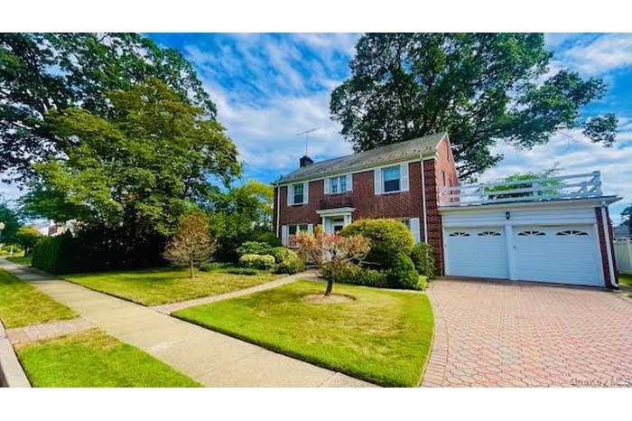 Colonial home with driveway, brick siding, a front lawn, and an attached garage