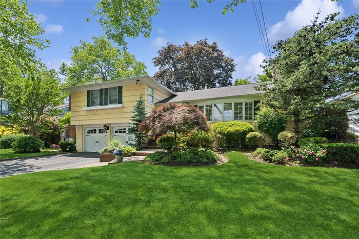 Split level home with driveway, a garage, a front yard, and brick siding