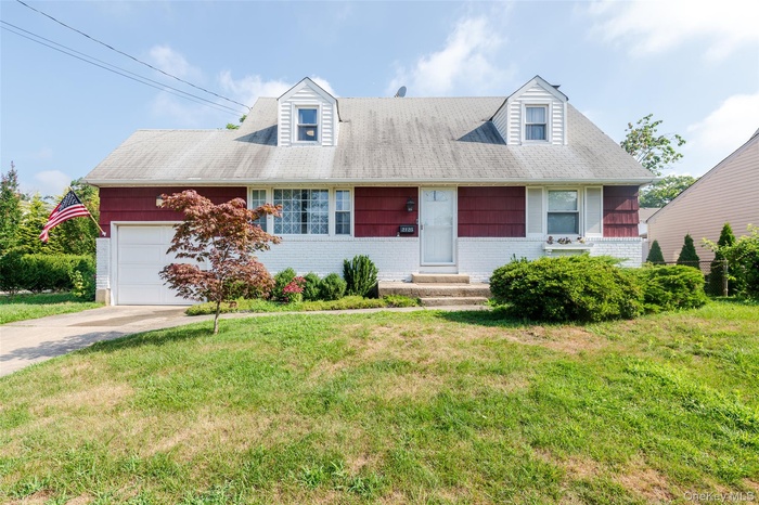 Cape cod-style house with an attached garage, a front lawn, and driveway