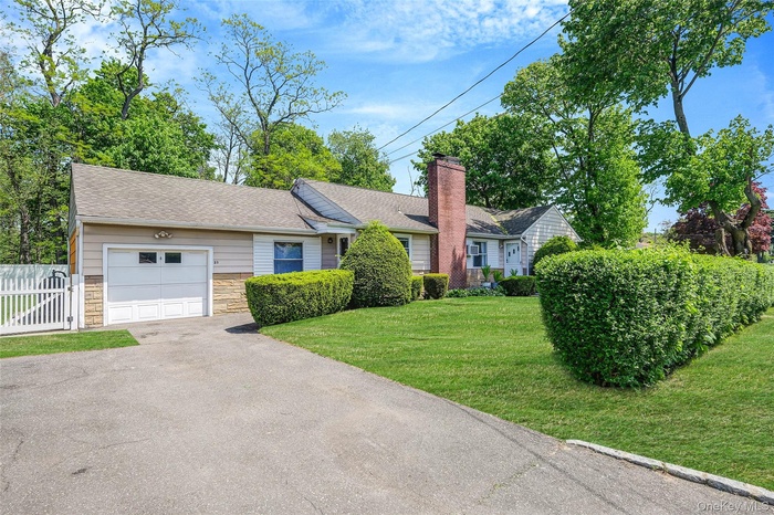 Ranch-style home featuring stone siding, driveway, a garage, a chimney, and roof with shingles