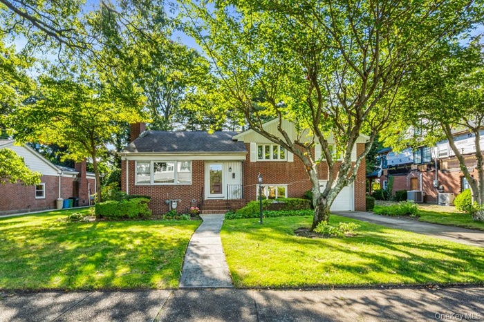 Tri-level home with brick siding, a garage, a front yard, a chimney, and driveway