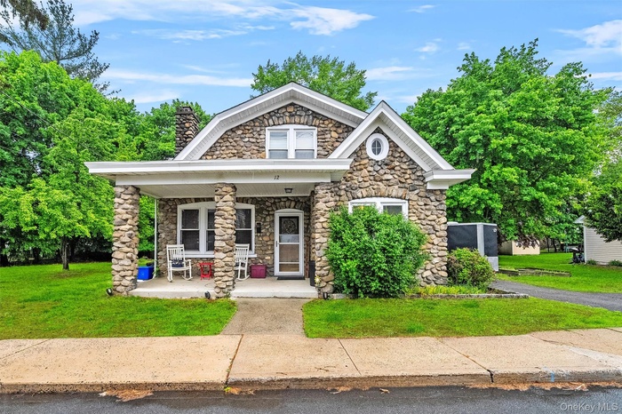 View of front of property featuring covered porch, stone siding, a front yard, and a chimney