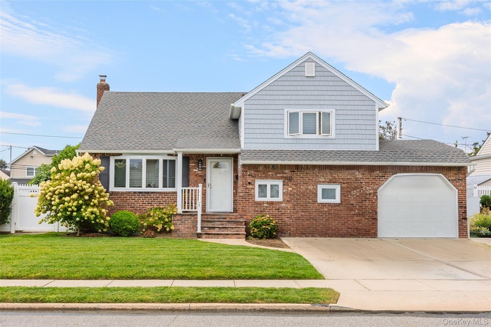View of front of house with a shingled roof, a front yard, a chimney, driveway, and brick siding