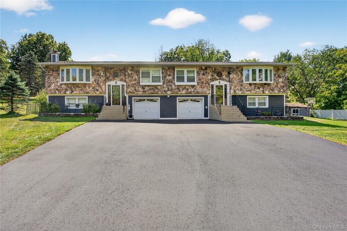 Split foyer home with stone siding, asphalt driveway, a chimney, and a garage