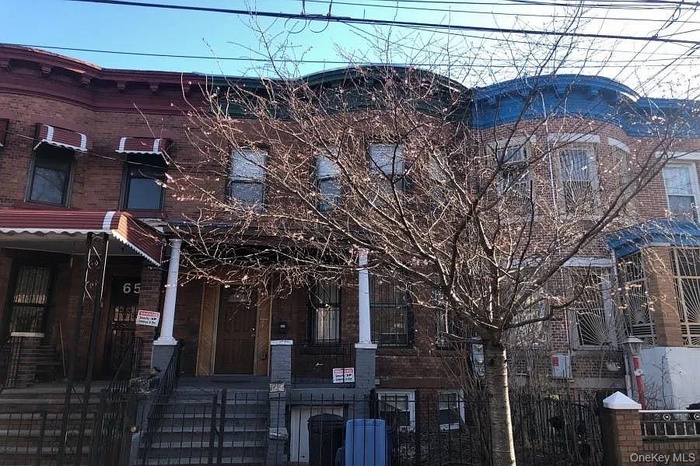 View of front of property with a fenced front yard, covered porch, a gate, and brick siding