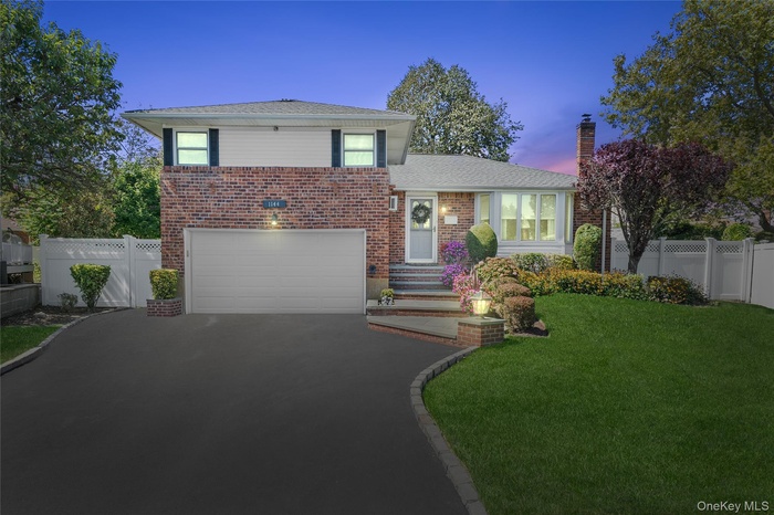 Tri-level home featuring asphalt driveway, brick siding, a garage, and a chimney