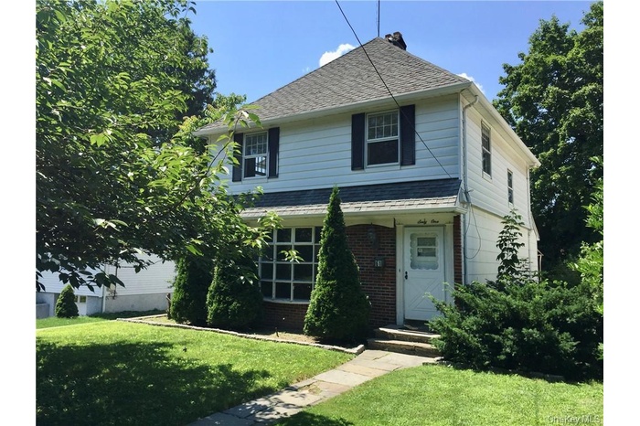 View of front of house featuring brick siding, a front lawn, and roof with shingles