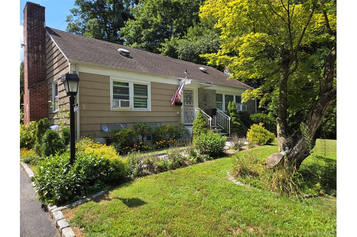 View of front of house featuring a chimney, a front yard, and a shingled roof