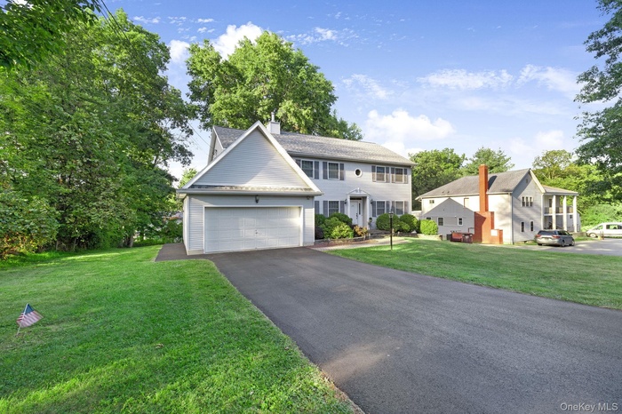 Colonial inspired home featuring driveway, a chimney, a front yard, and an attached garage