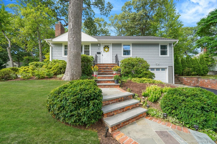 Ranch-style home featuring an attached garage, a chimney, a front lawn, and a shingled roof