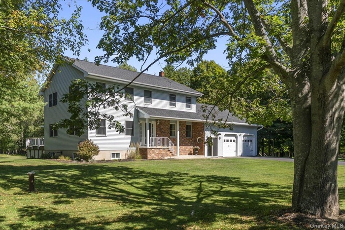 Traditional-style home featuring a front lawn, a chimney, brick siding, a porch, and asphalt driveway